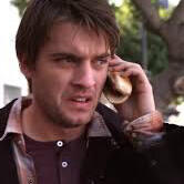 a screenshot of chase williamson portraying dave in the john dies at the end movie. his expression is confused or disgusted as he holds a hot dog to his ear